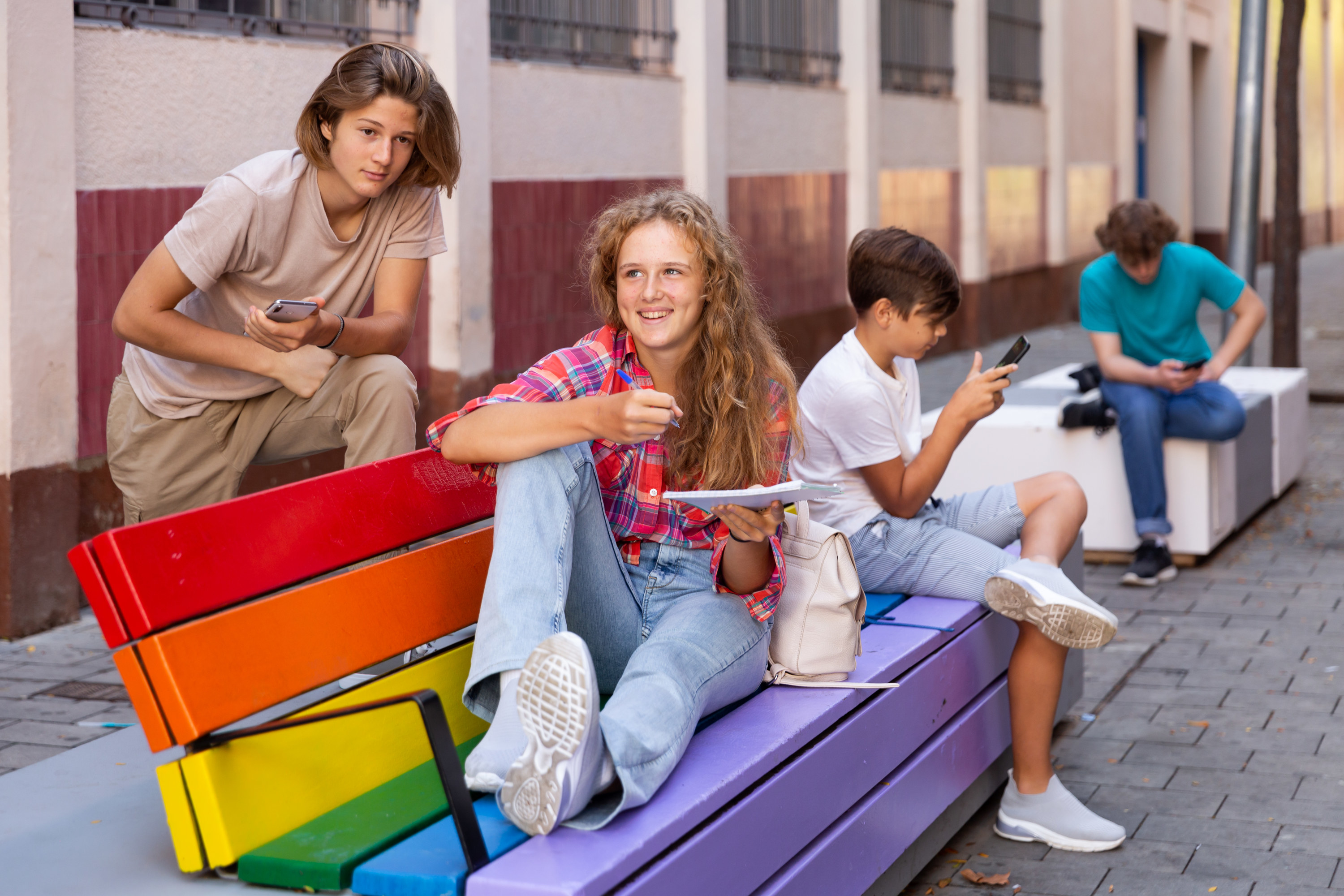 Three kids siting on a rainbow colored bench hanging out with each other