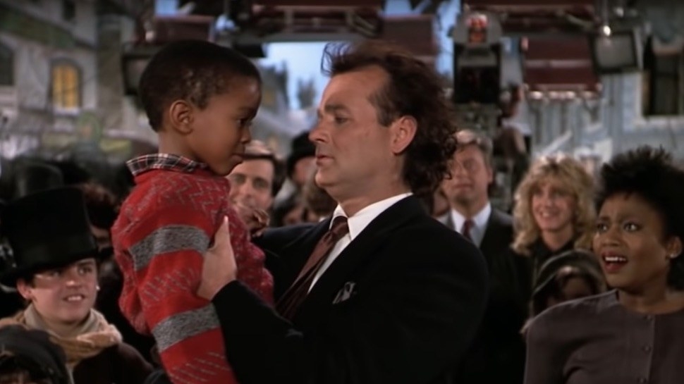 bill murray as frank in scrooged holding calvin as the crowd smiles at them