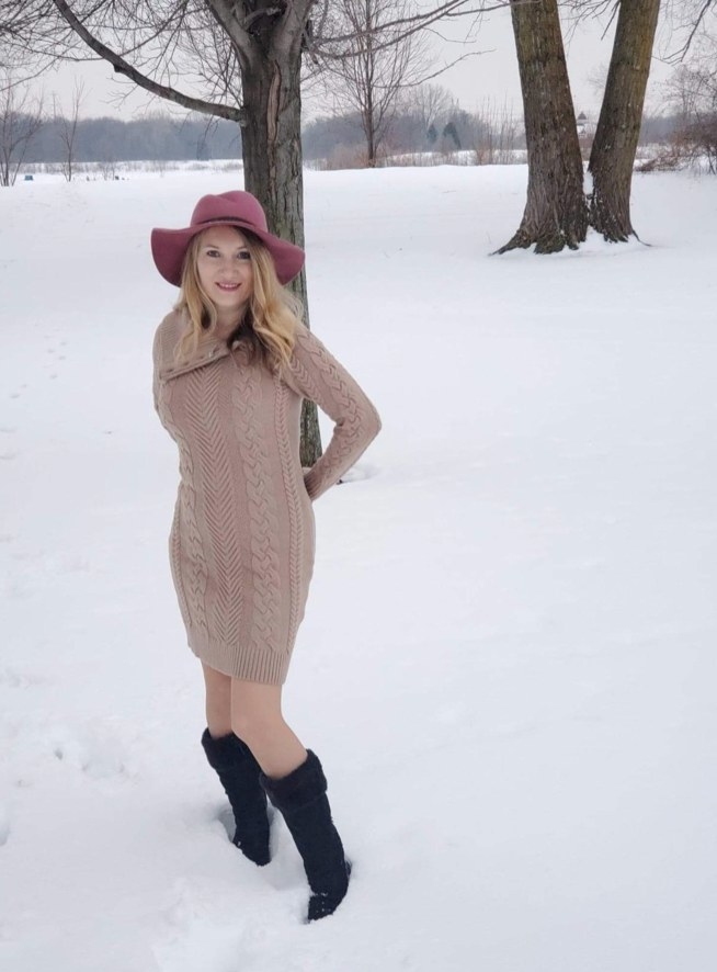 A reviewer wearing the dress in tan with red hat and black boots