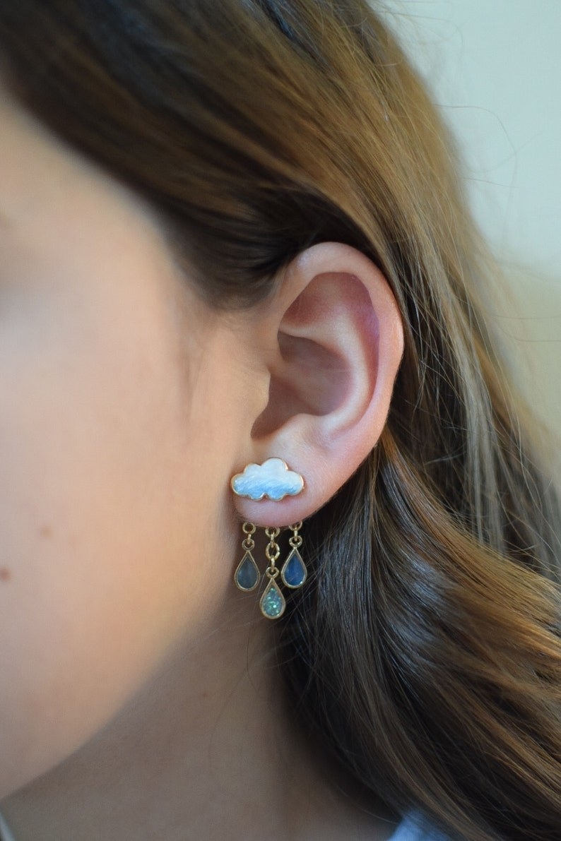 model wearing the earrings, with a cloud stud in front of the lobe and fringed raindrop jewels in back