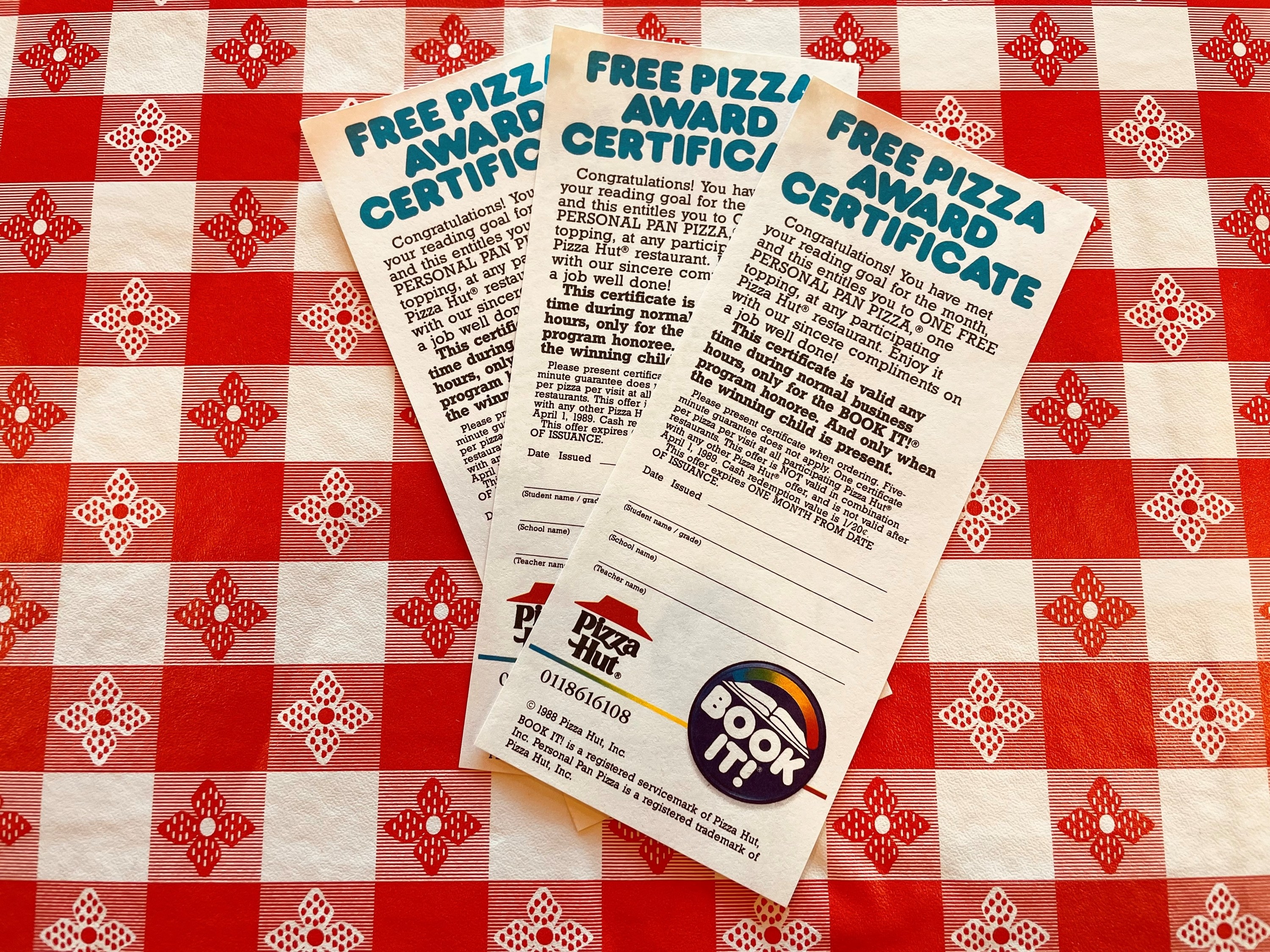 Three Pizza Hut reading award certificates fanned out on a checked tablecloth