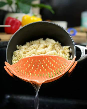 Pot of pasta being strained through orange clip-on colander