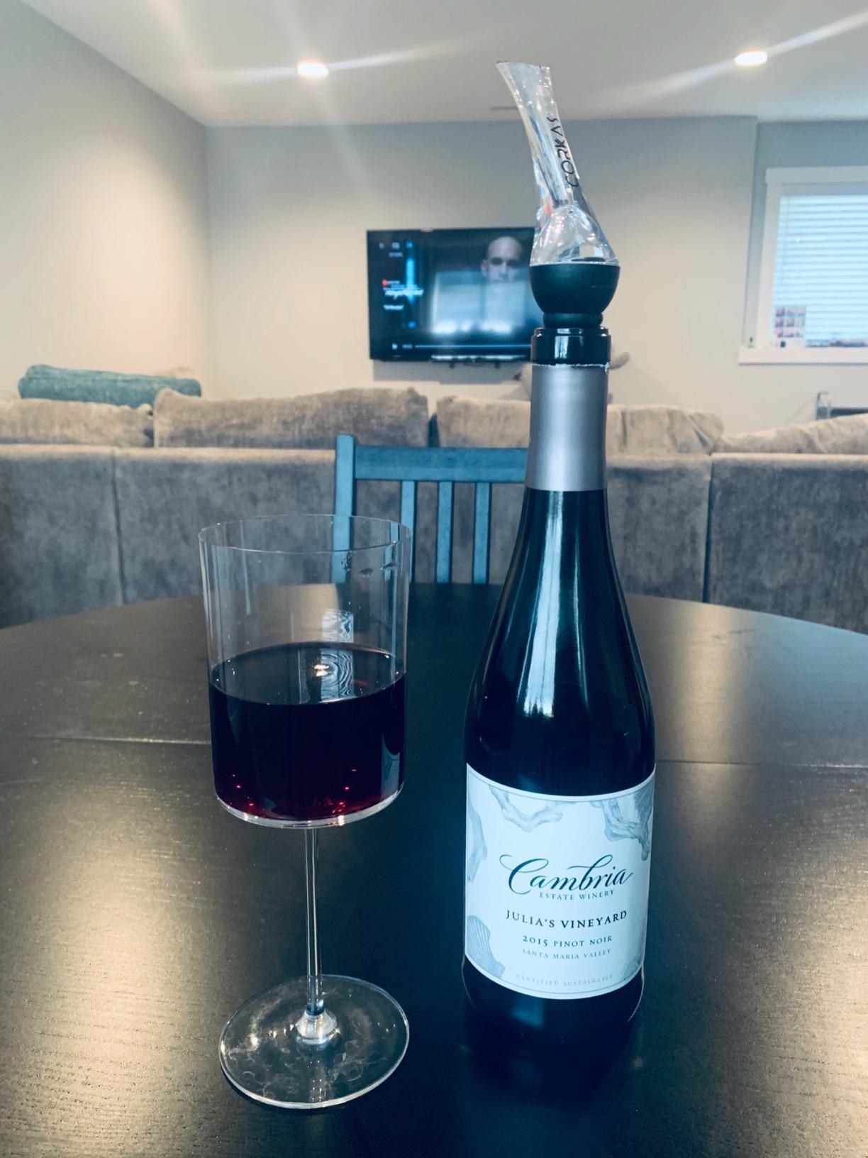 bottle of wine with the aerator plugged into the top and a glass of wine beside it