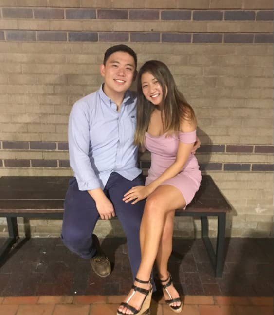 A smiling couple sit on a bench, posing for a photo