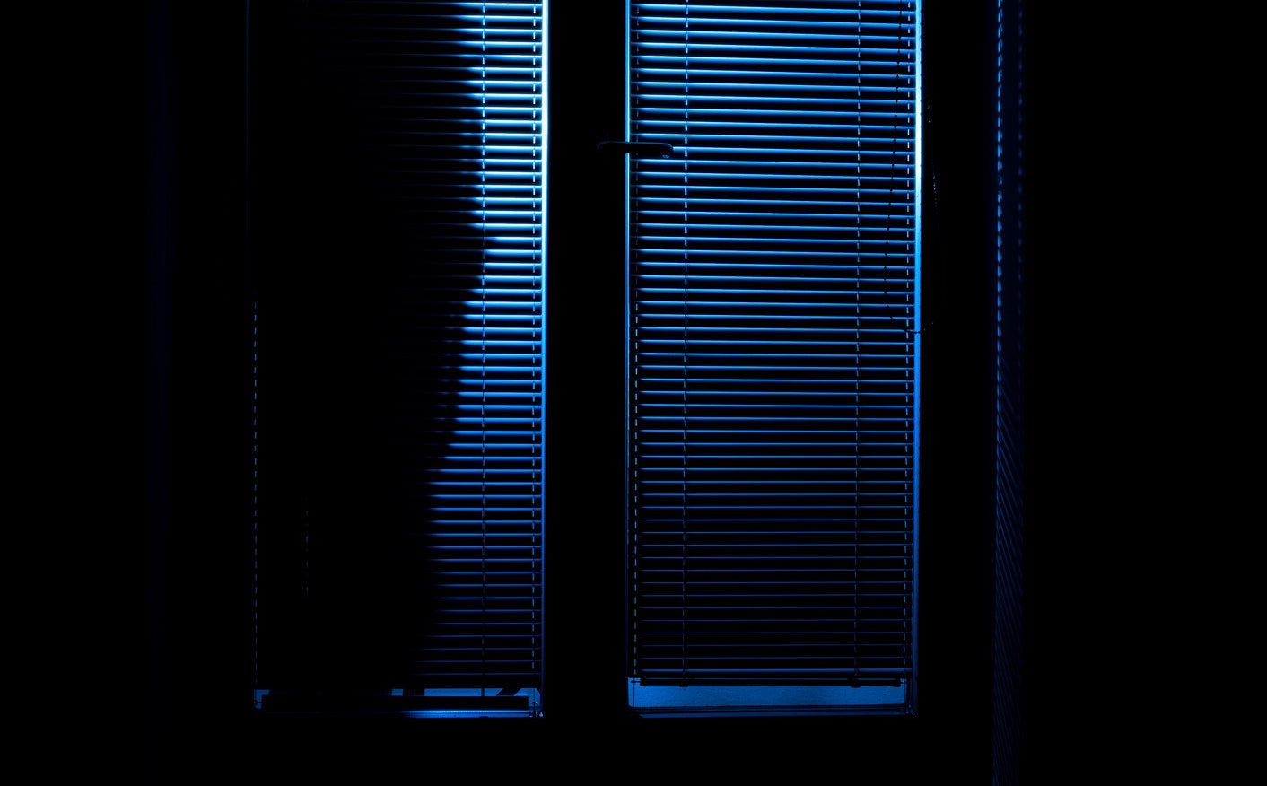 Silhouette of a person outside of a door with blinds closed at night