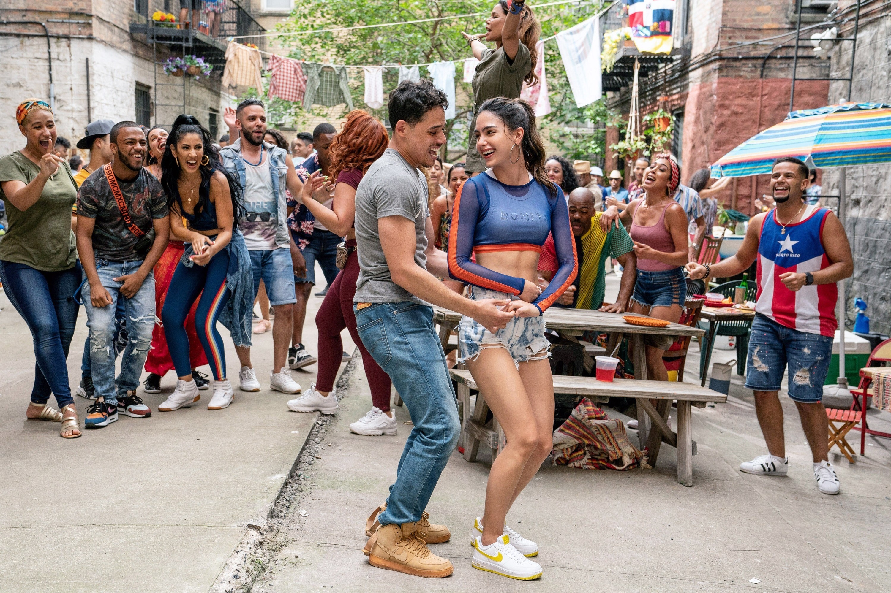 A Latin man and woman dance together in the street. A crown of Latin men and women cheer them on and dance