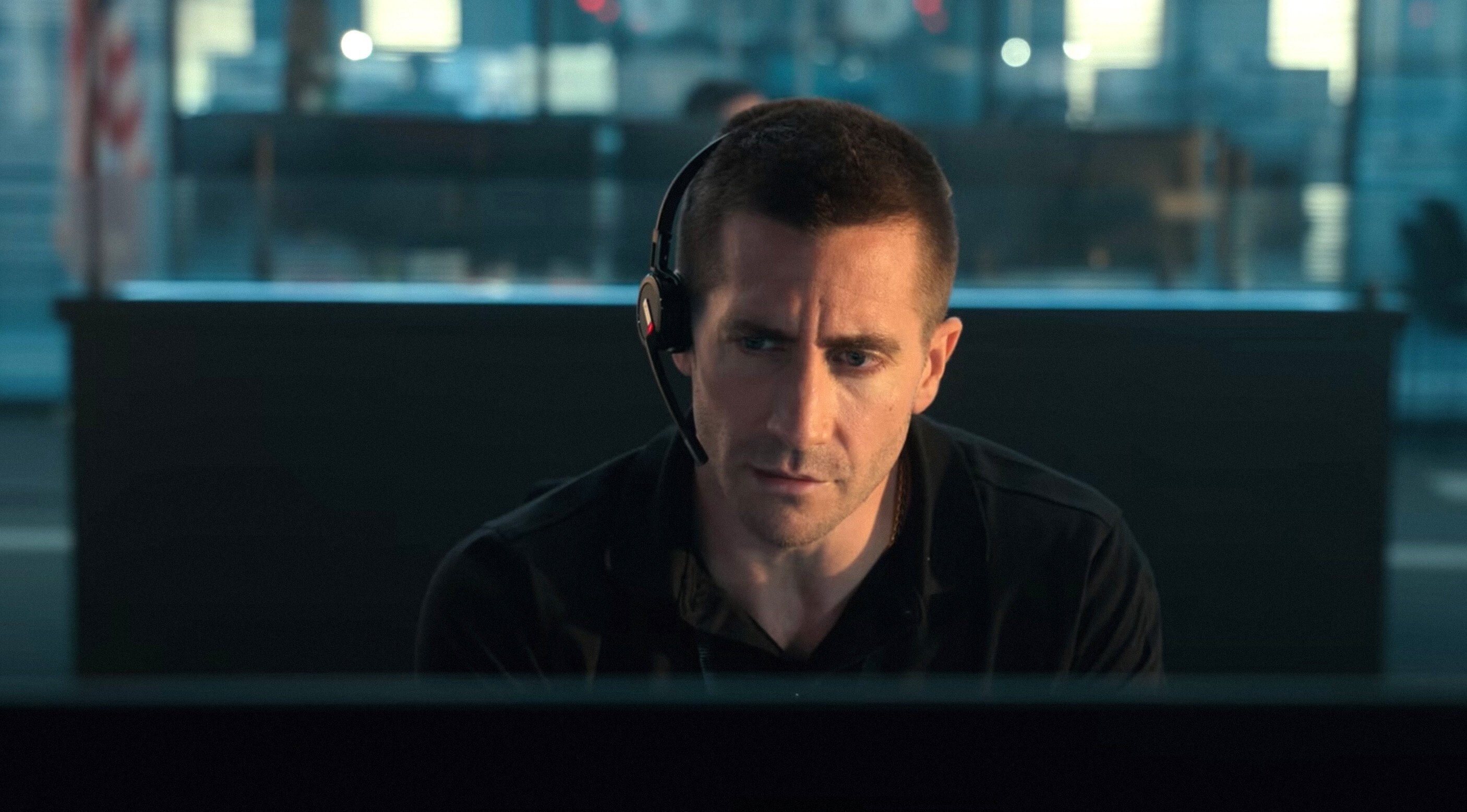 A white man with short brown hair sits wearing a headset. He looks down at a screen concerned.