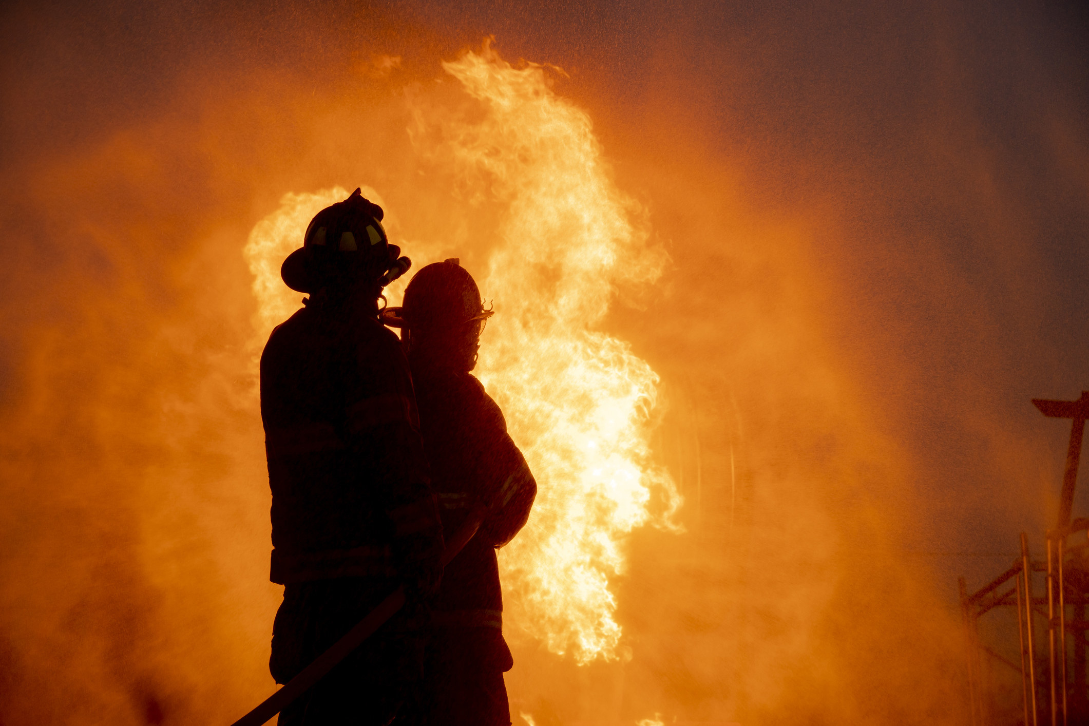 Silhouette of two firefighters in front of a big fire
