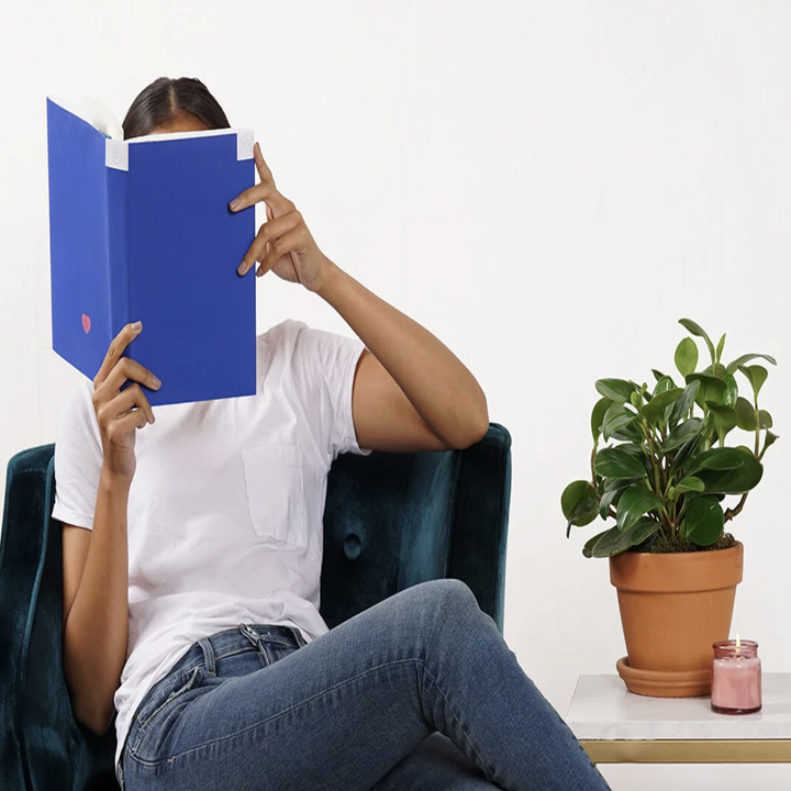 model reading a book with blue cover next to potted plant