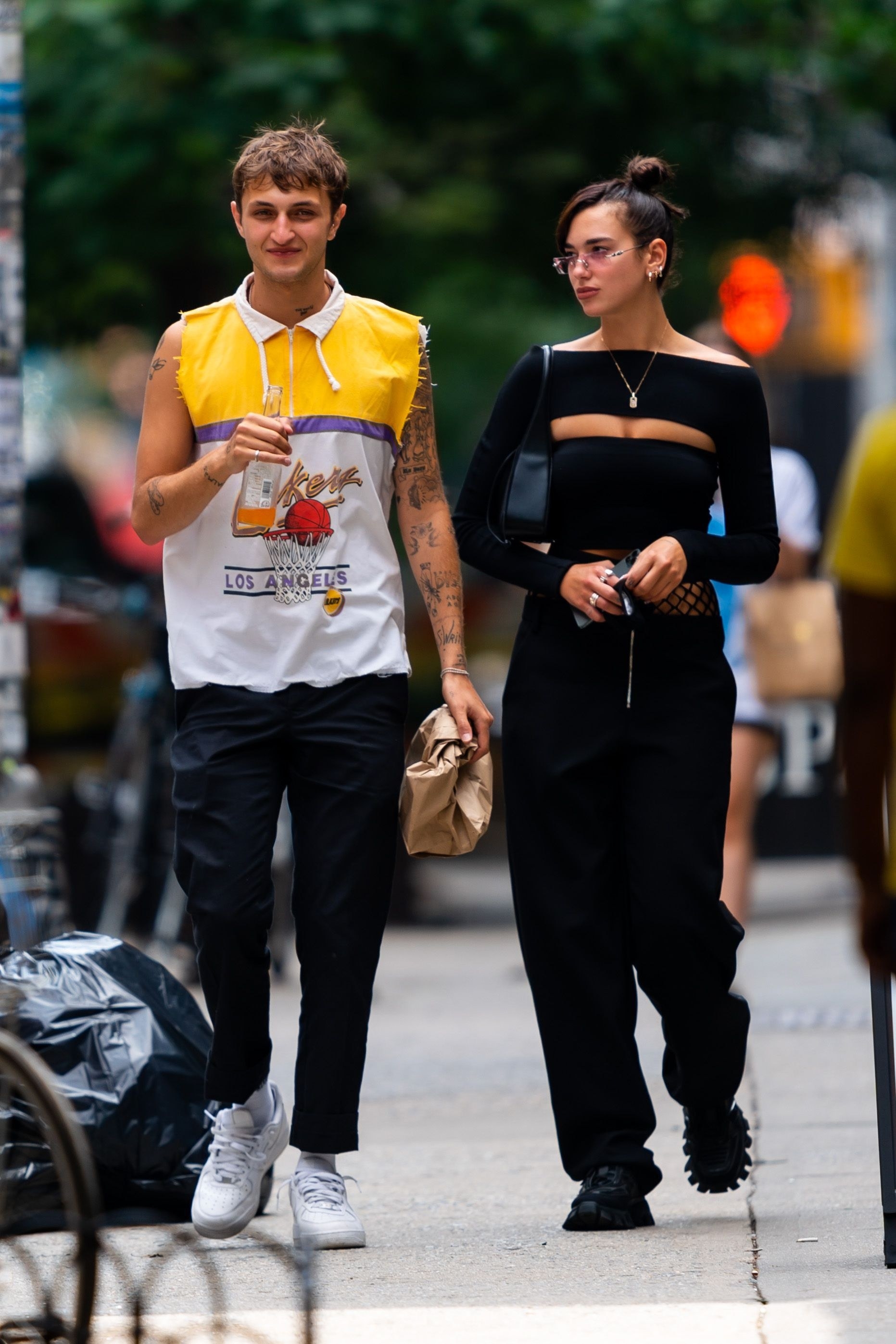 Anwar holds a bottle of orange soda while walking next to Dua in the street