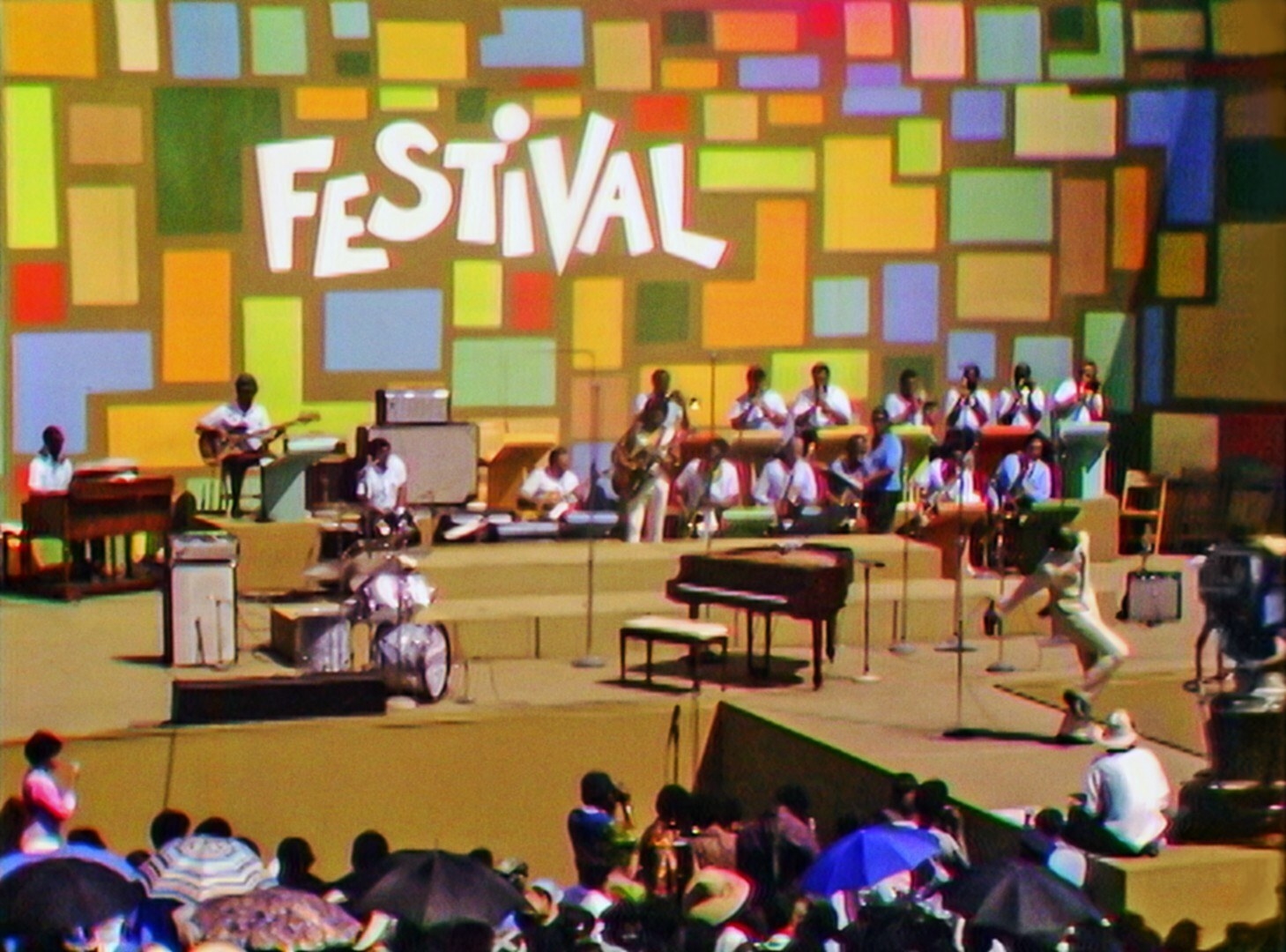 A stage at the Harlem Culture Festival in 1969. The stage is colorful with a backdrop of colorful squares with the word "Festival." A band performs