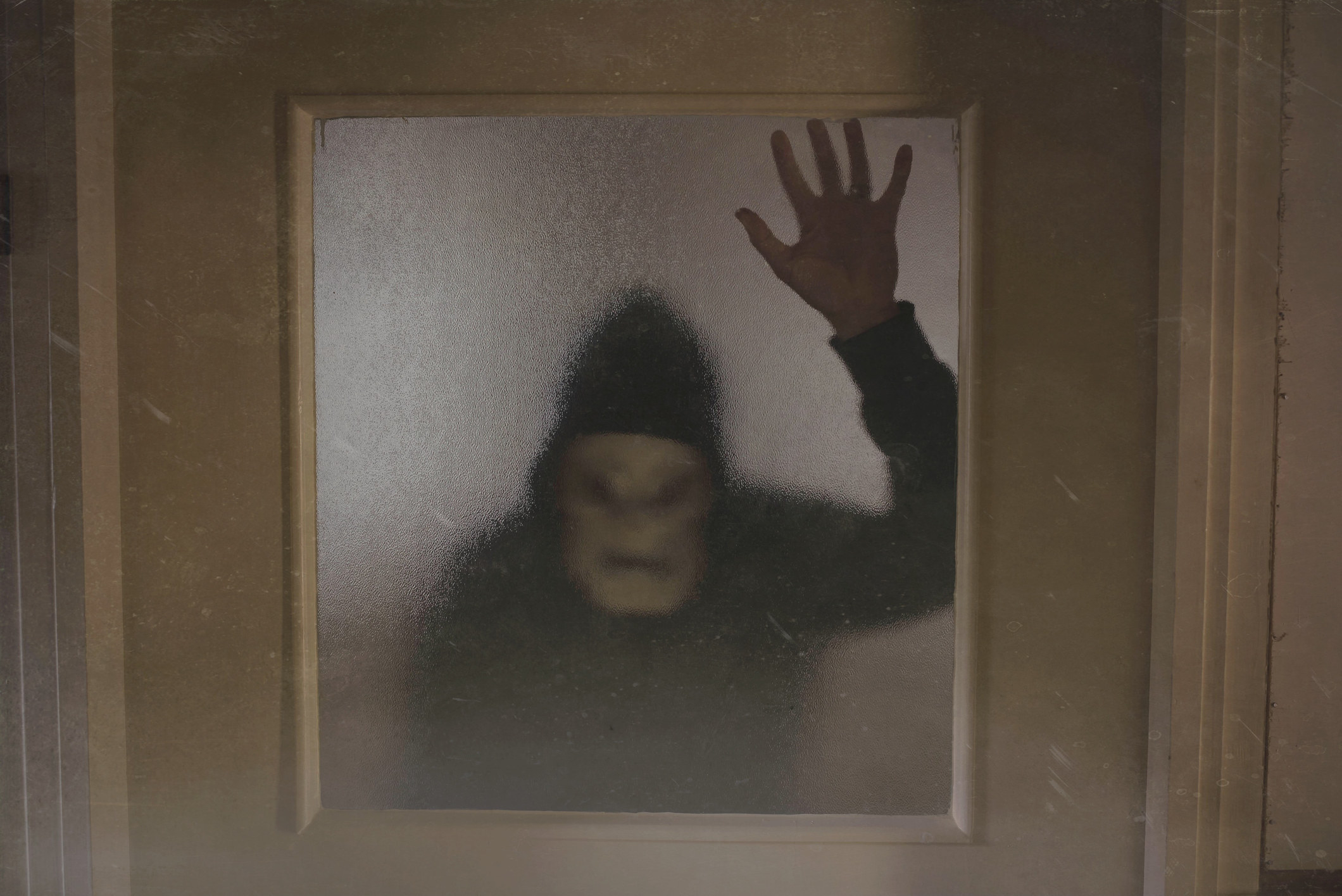 Person wearing spooky mask and hoodie is seen through the glass of a back door
