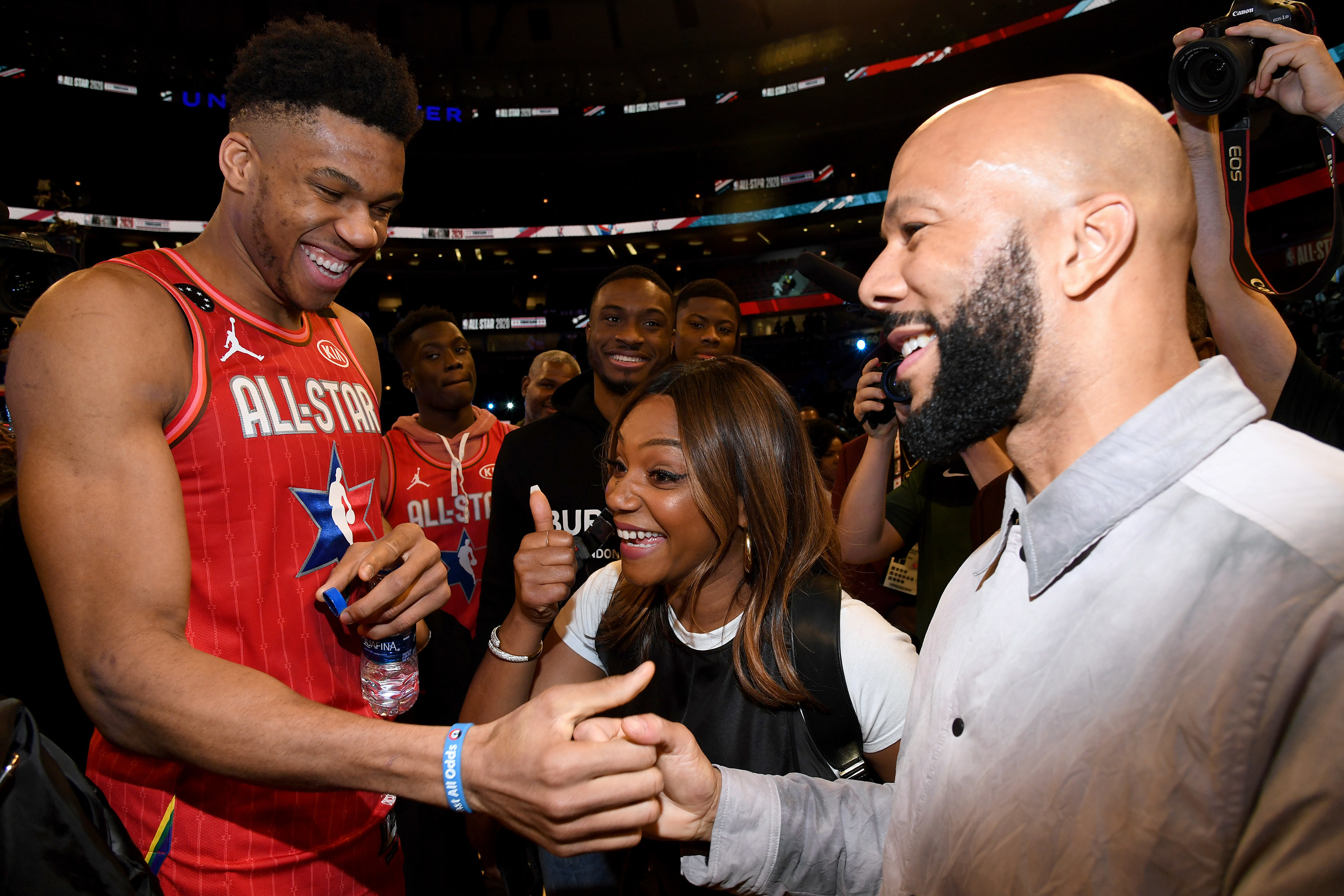 Tiffany gives a thumbs up while Common and Giannis Antetokounmpo clasp hands at a basketball game