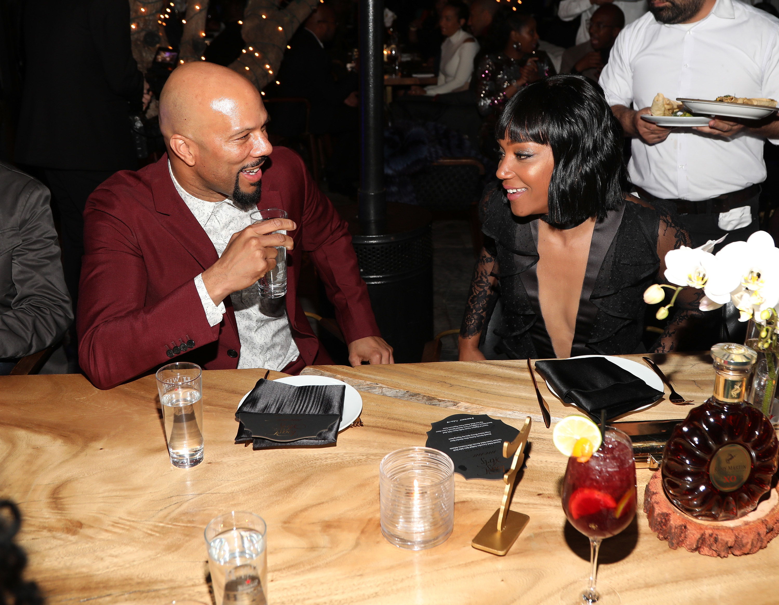 Common and Haddish talk at a table while he holds a glass
