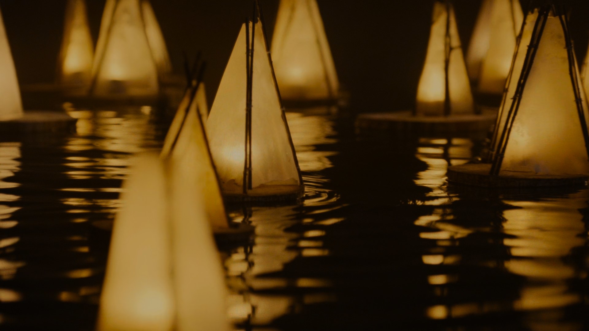 A night-time shot of many triangular lanterns, each with a candle inside, floating down the Taren river on a disc of wood