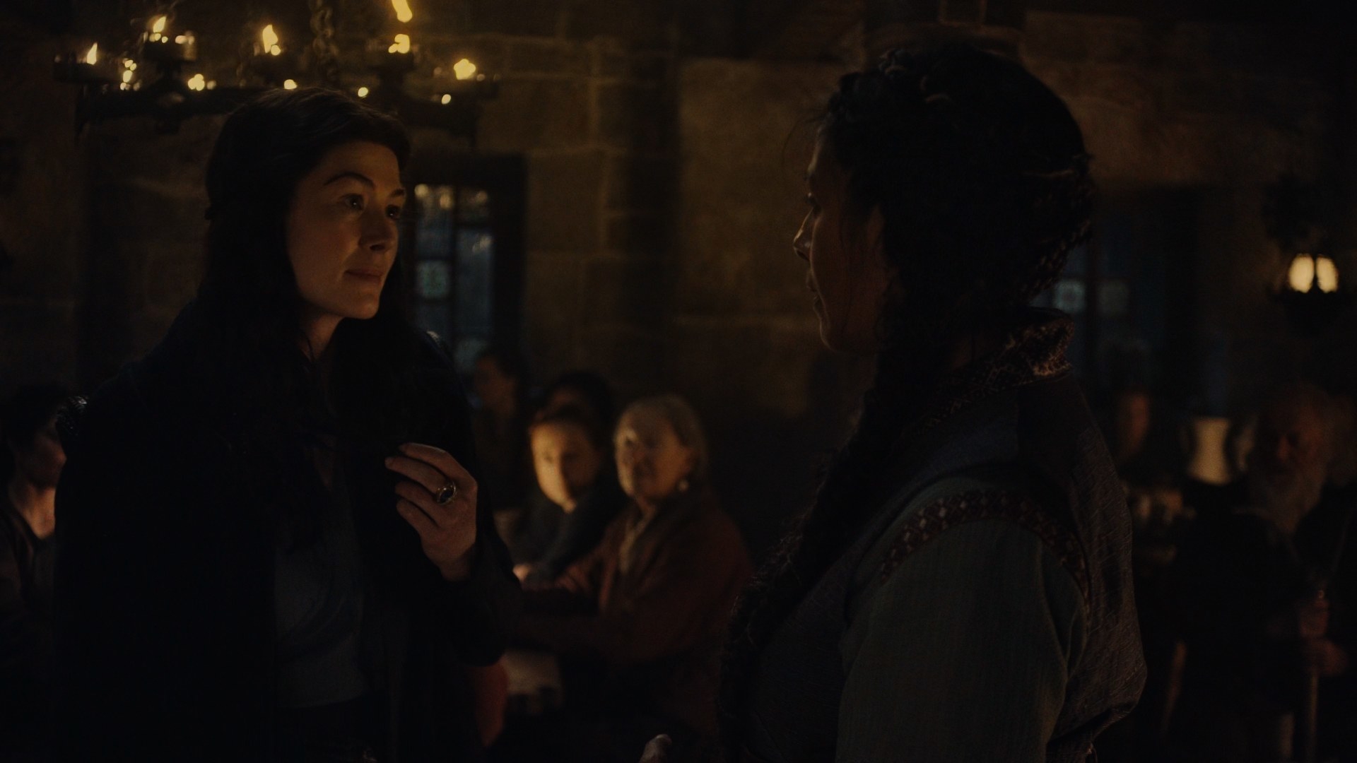 A medium-shot showing Moiraine and Marin al’Vere (Lolita Chakrabarti) in the crowded Winespring Inn. Moiraine’s Aes Sedai ring is on full display as she twists her hair around her fingers