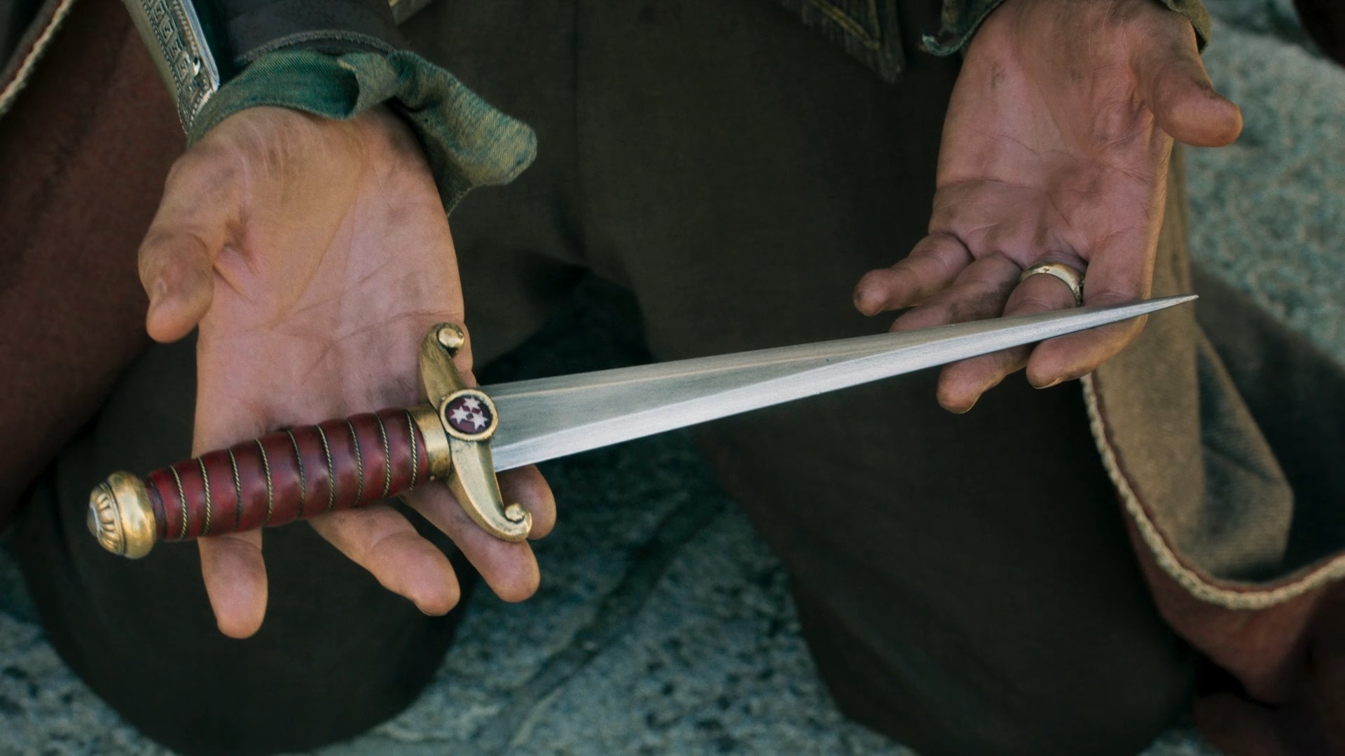 A close-up shot on Logain’s hands, offering up a gold-and-red dagger with the three stars of Ghealdan on the hilt