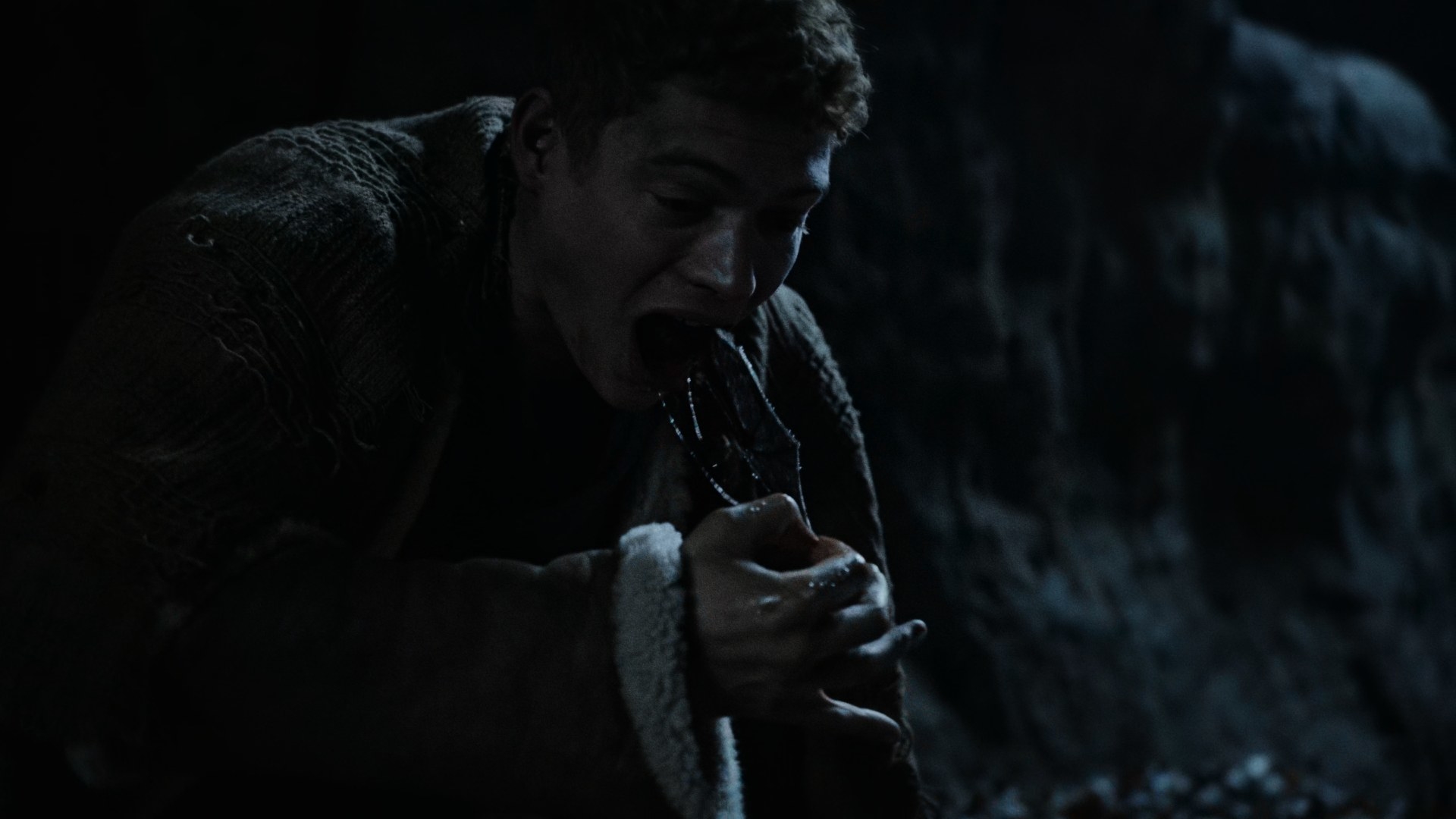 A medium shot of Rand at night outdoors, pulling a large dead bat out of his mouth, gagging as he does so