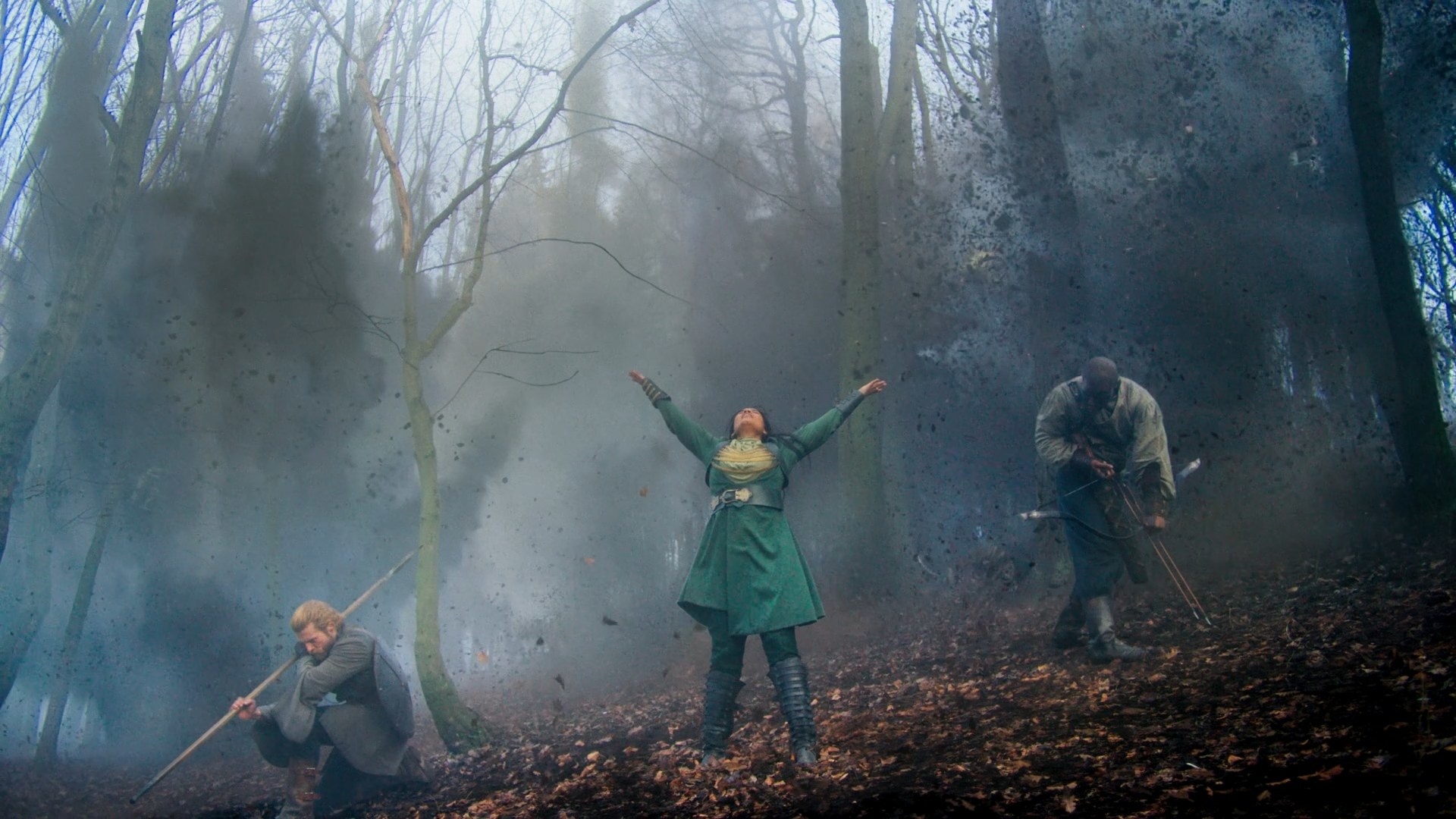 Alanna (Priyanka Bose) has her arms flung wide and her head pulled back in a shout as she uses the One Power to create massive explosions in the woods around her. She is flanked by her warders, Maksim and Ihvon, who are bracing themselves