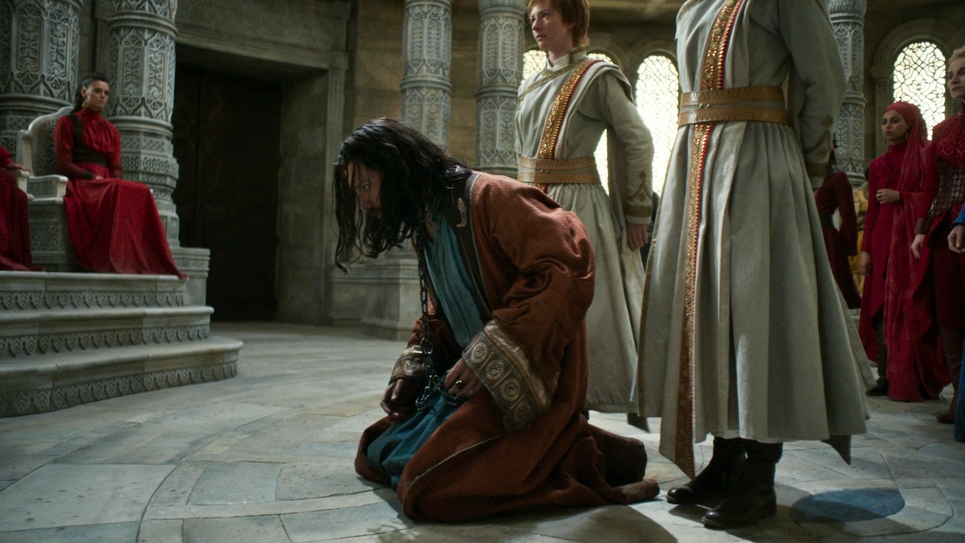 A shot of Logain in chains being forced to his knees in the Hall of the Tower by white-and-gold robed Tower Guards