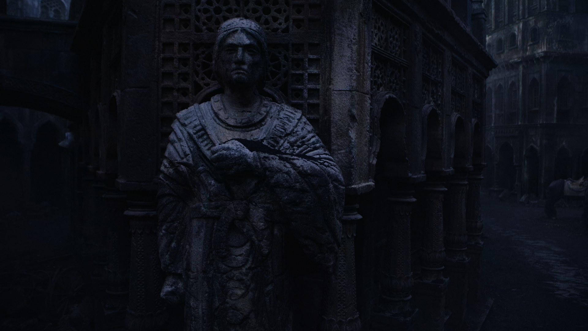 A shot focusing on a weathered statue in Shadar Logoth. It depicts a man with a stern face, his left arm pulled across his chest. Visible in the carved belt is a dagger with a stone in the hilt, and two prongs.