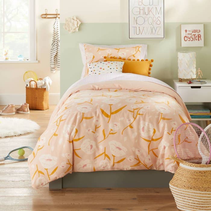 A kid&#x27;s room with a pink and orange floral bed spread on a full bed