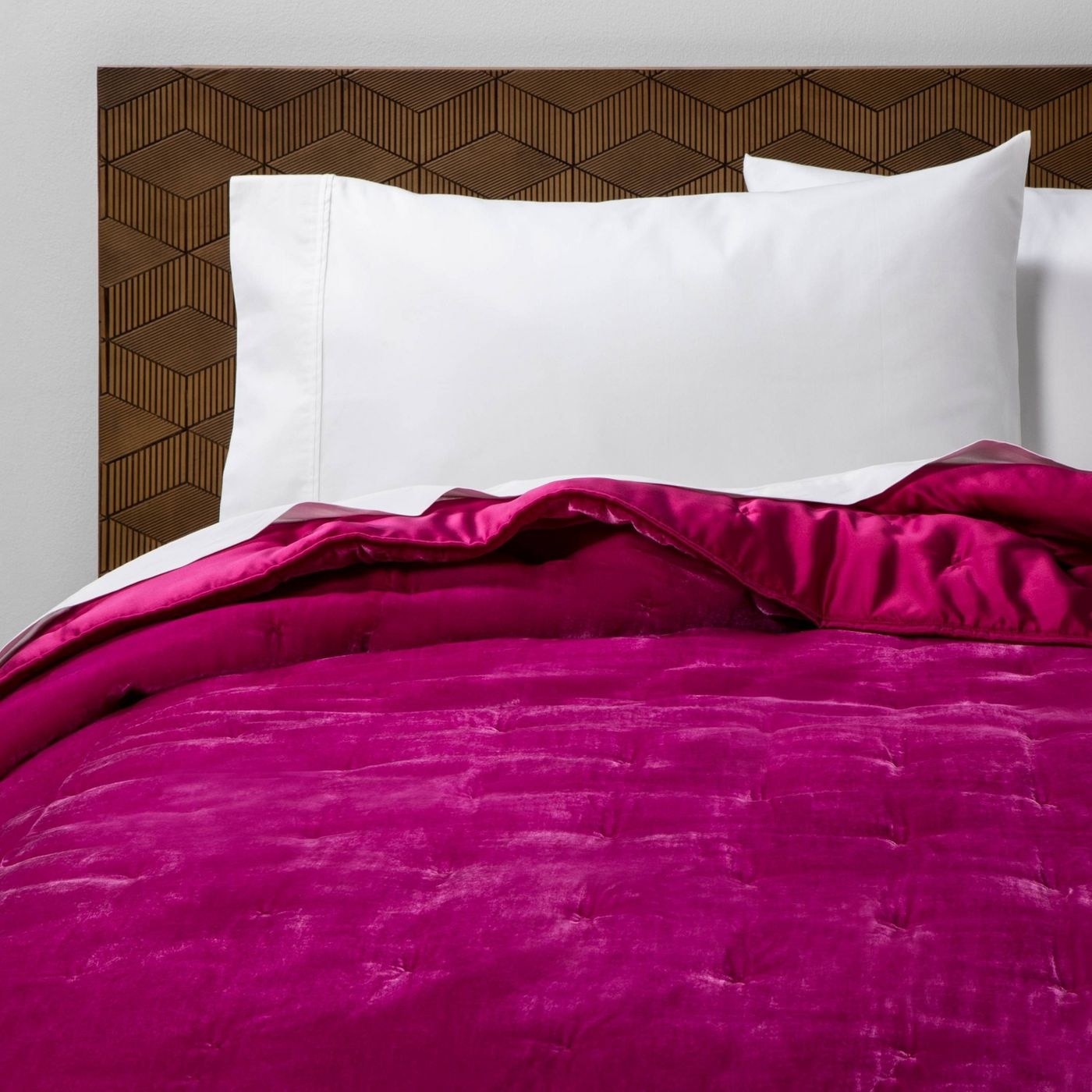 A velvet fuchsia quilt on a brown bed.