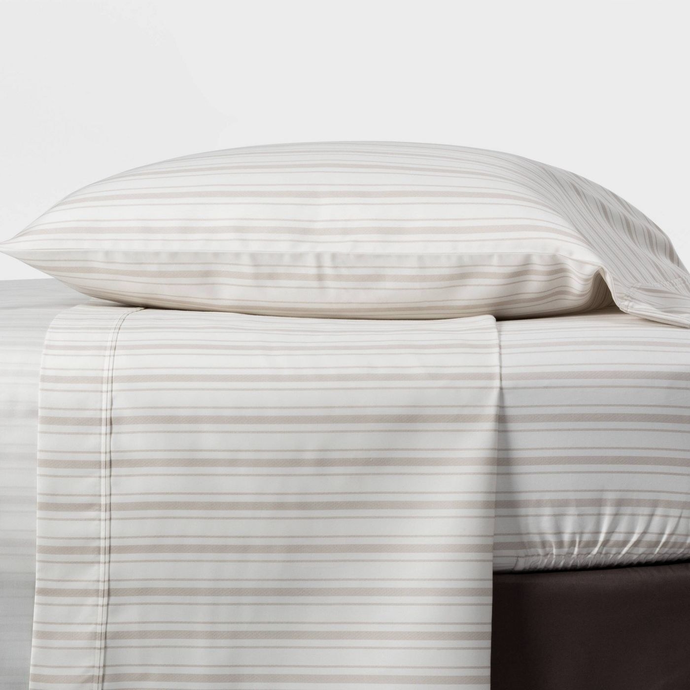 A bed sheathed in a white and pink striped sheet with a pillow on top in a matching case