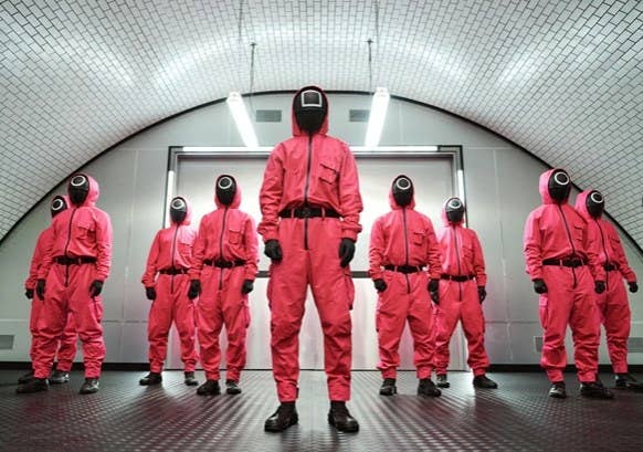 A group of Squid Game guards stand in their red suits and masks at the entrance to the dorm
