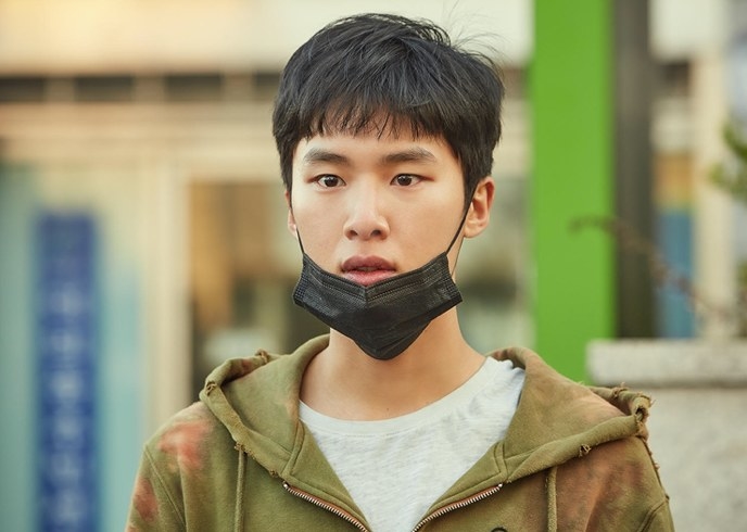 A teen boy wears a surgical mask on his chin and dirty clothes