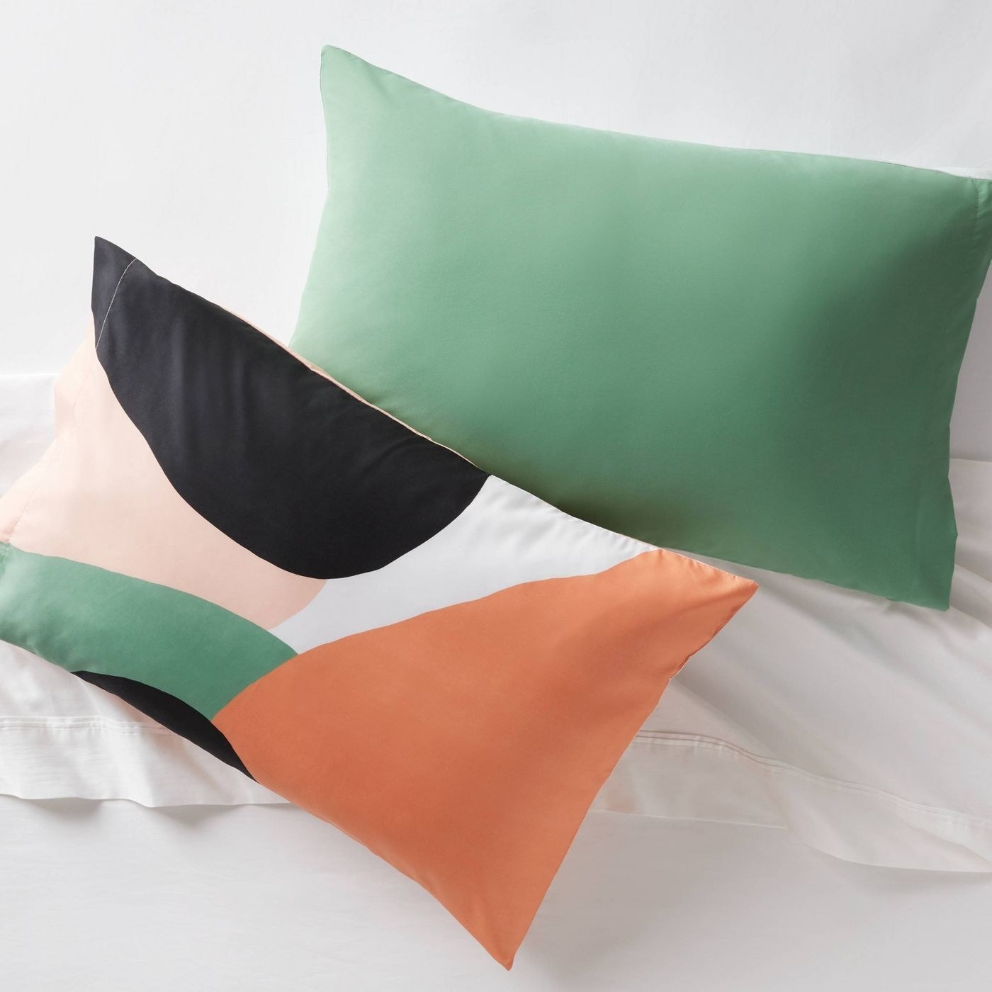 A green pillow and a pillow with orange, green, pink and black blobs