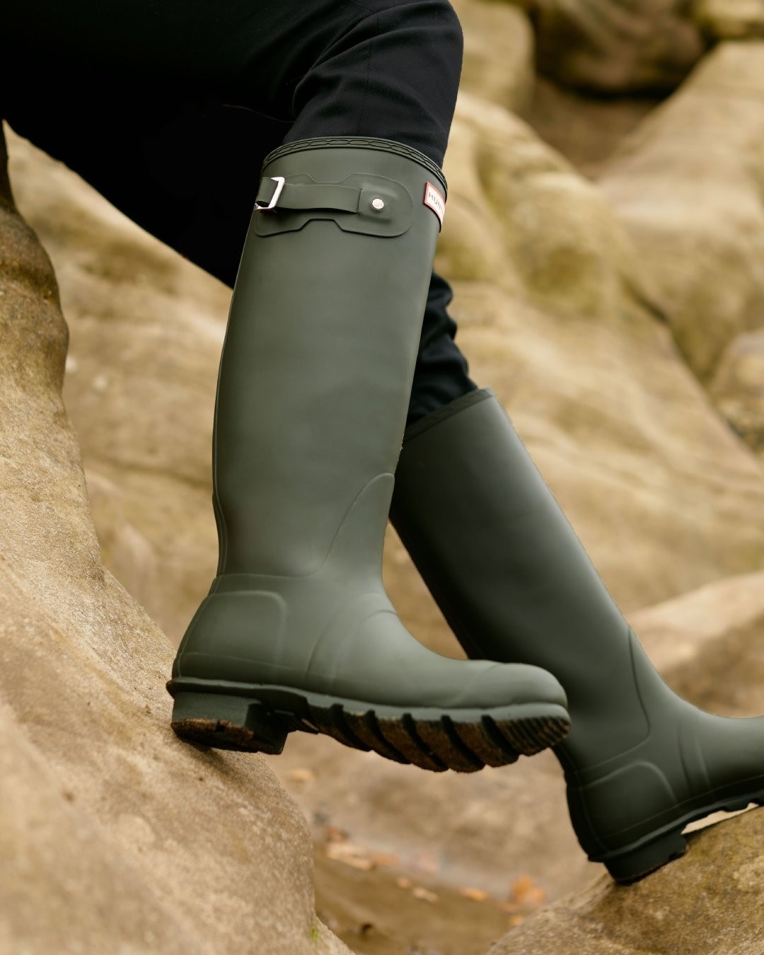 A person wearing a pair of Hunter boots while climbing on a rocky trail