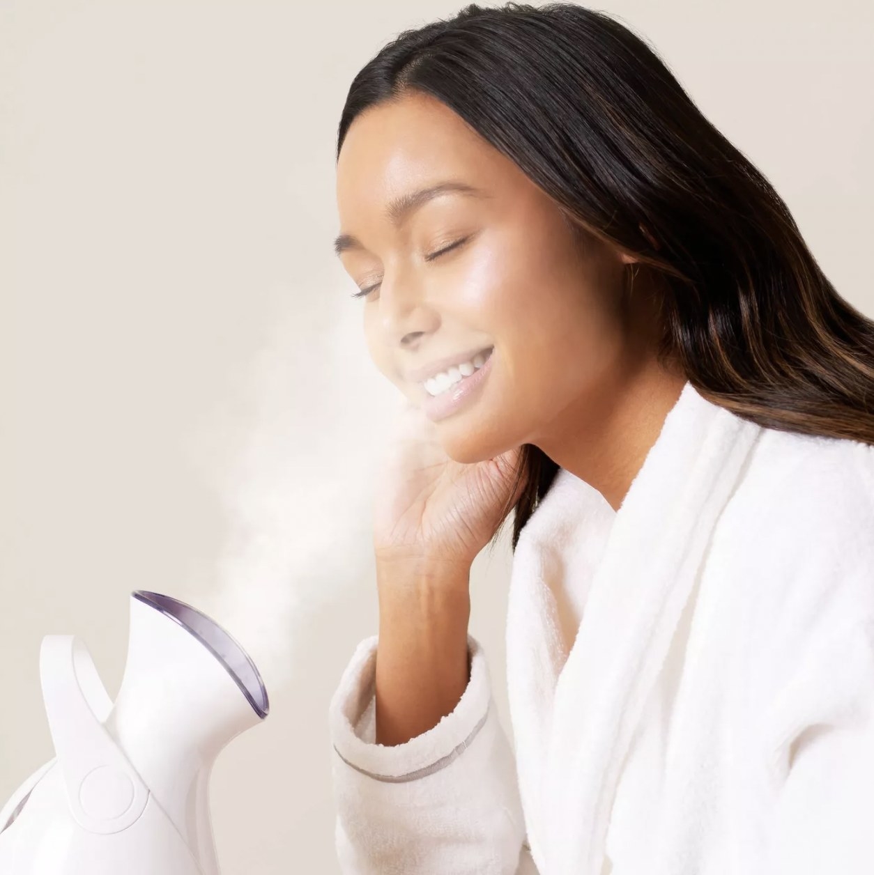 Women using facial steamer in white robe