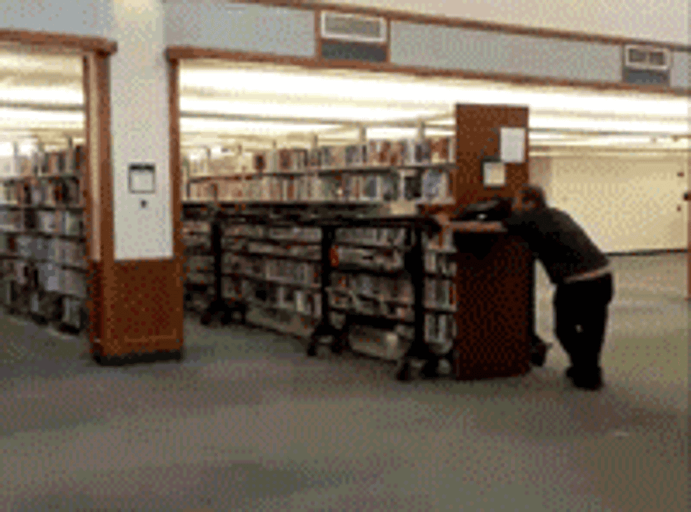 ID: two people carry a huge shelf of library books
