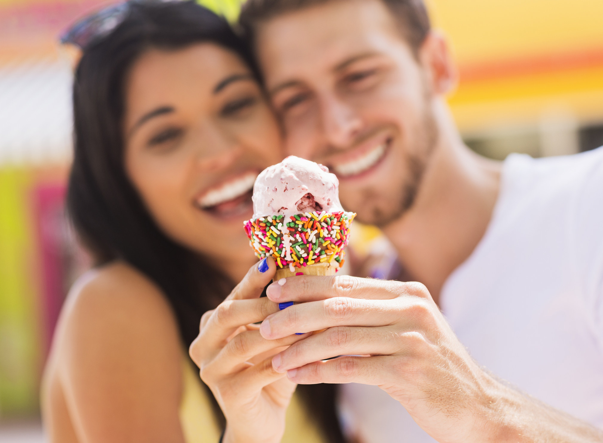 A couple holds a dripping ice cream cone they&#x27;re sharing close to the camera