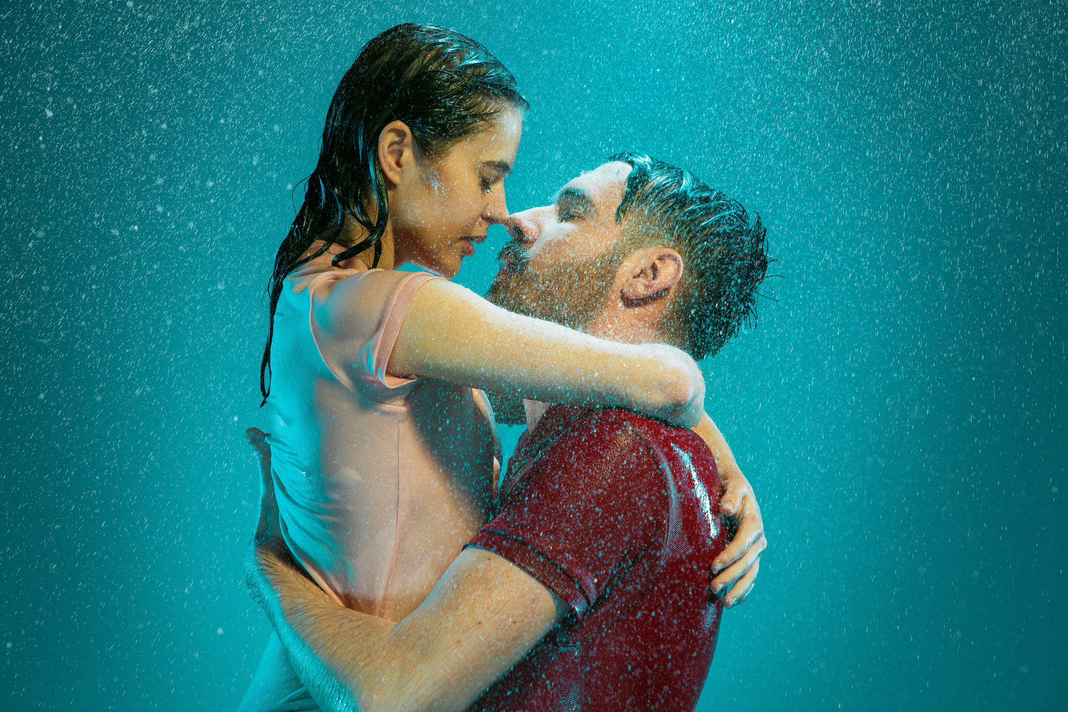The loving couple kissing in the rain on a turquoise background