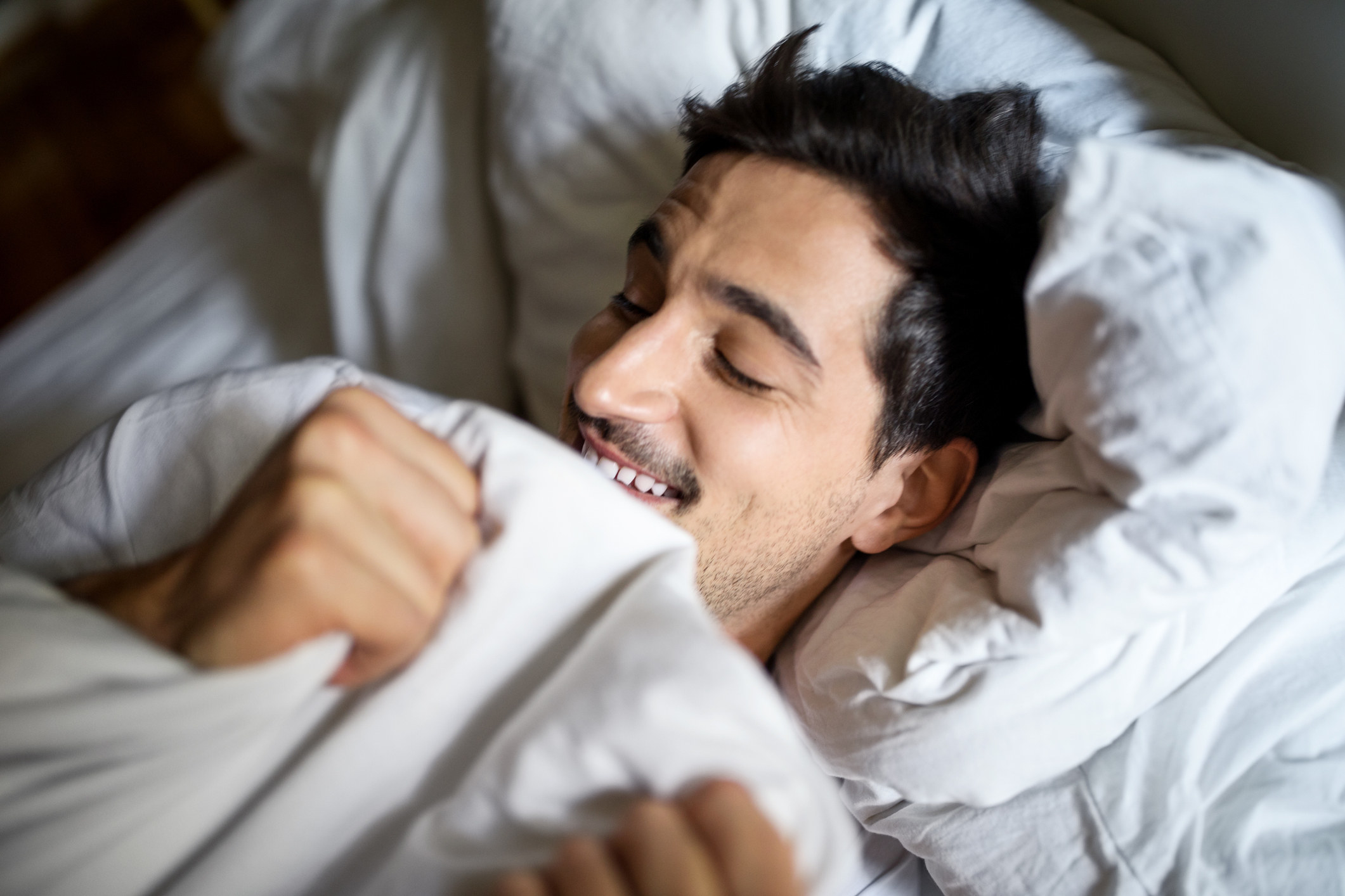 Smiling young man sleeping comfortably in bed at home