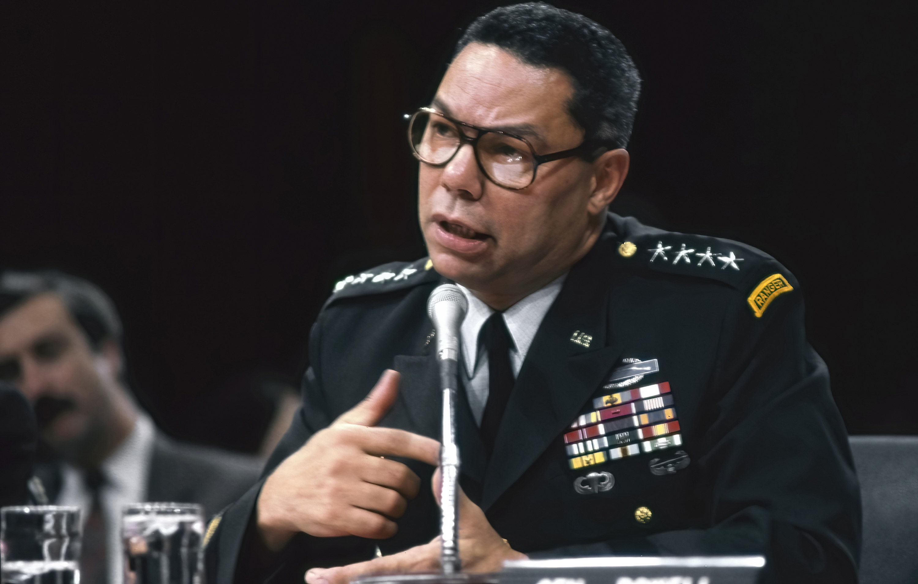 Colin Powell in uniform testifying in congress in front of a microphone