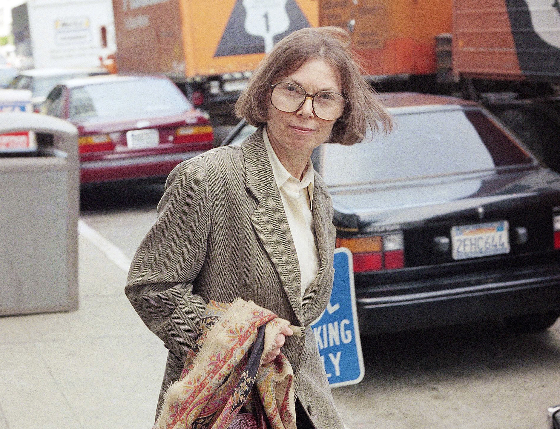 janet malcolm in a suit carrying a scarf on a street 