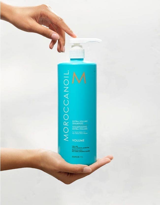 hands hold blue liter bottle of Extra Volume Shampoo