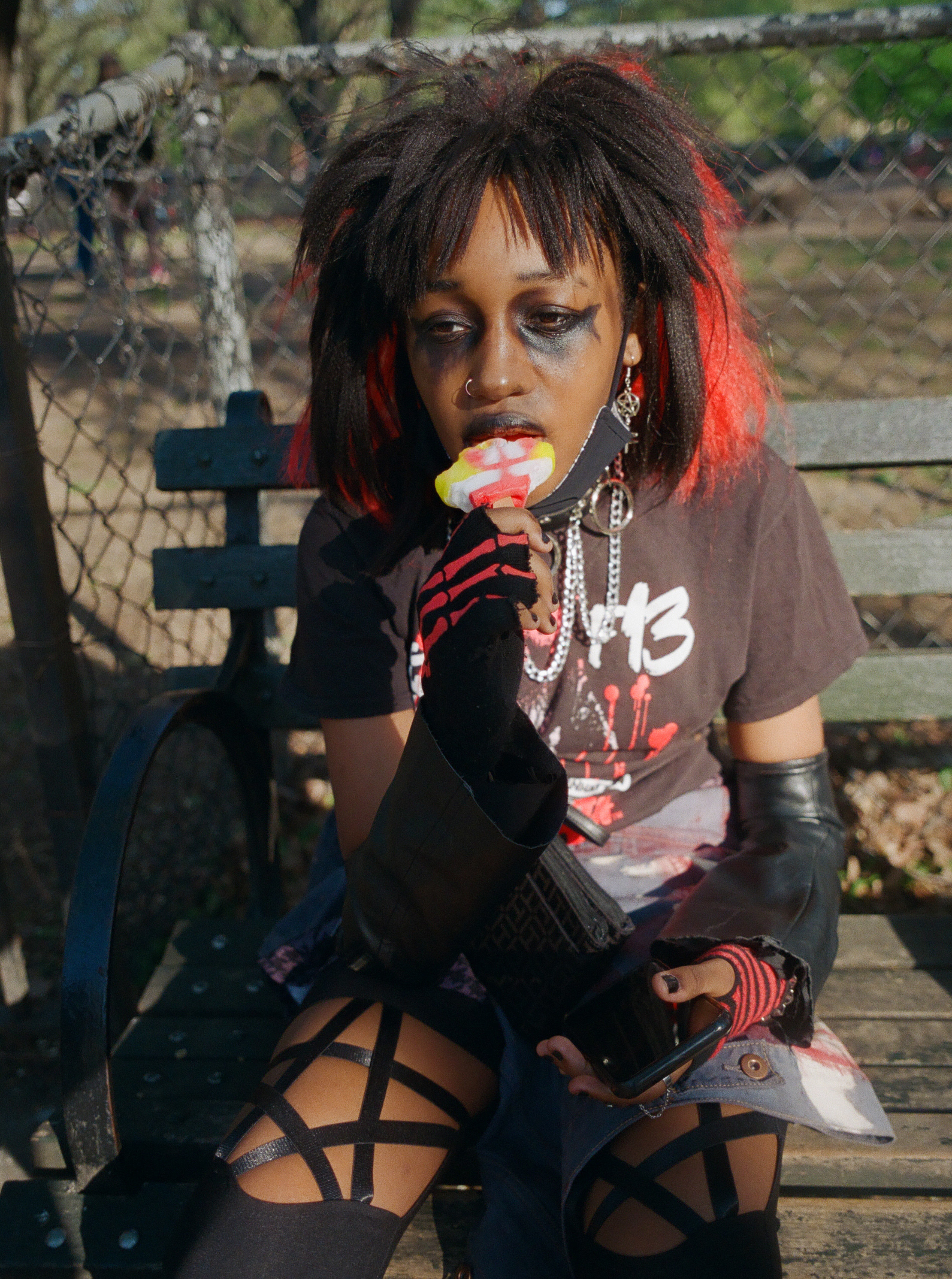 a young goth girl eats a spongebob ice cream on a park bench 