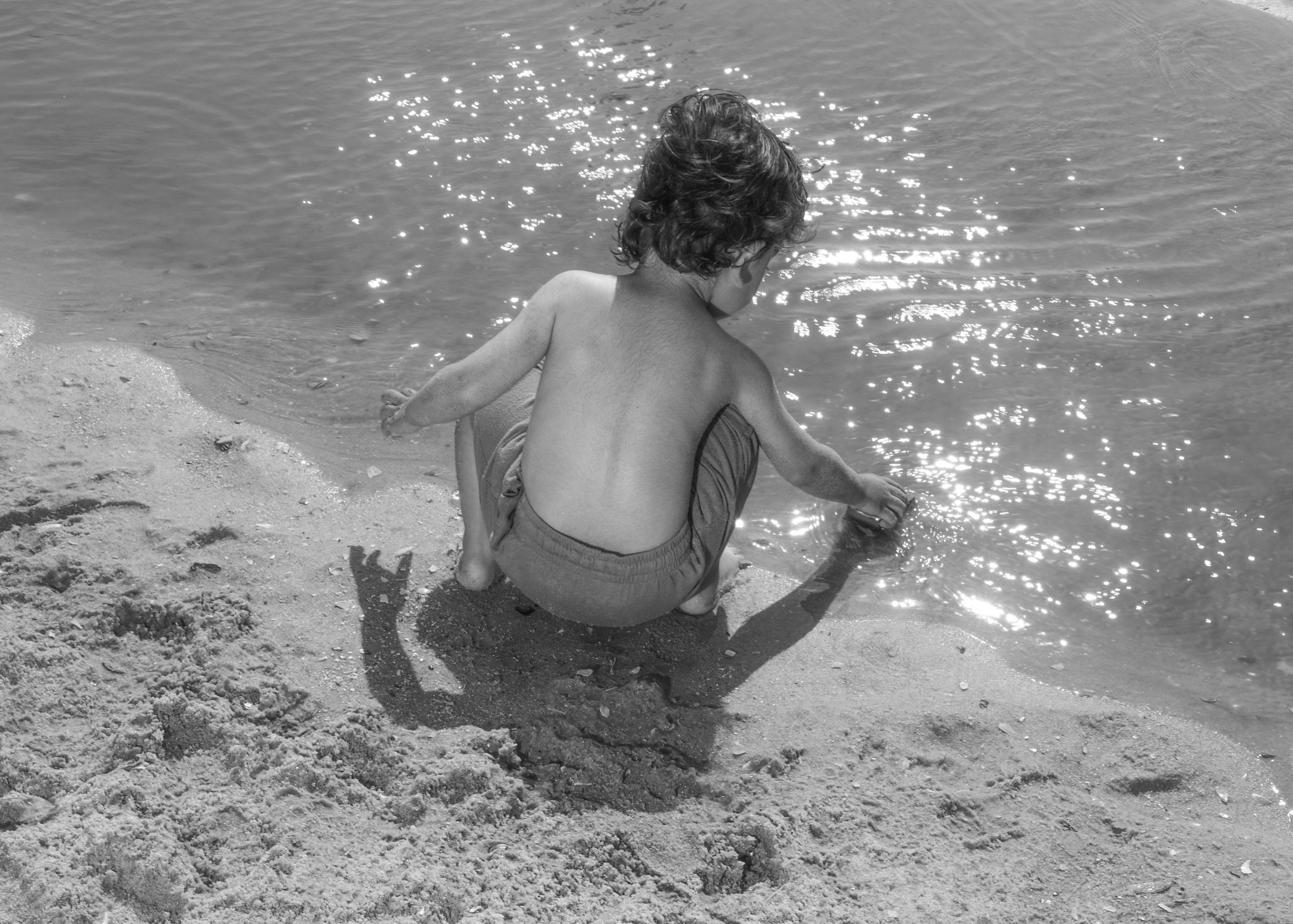 A young boy plays in the sang at the water&#x27;s edge