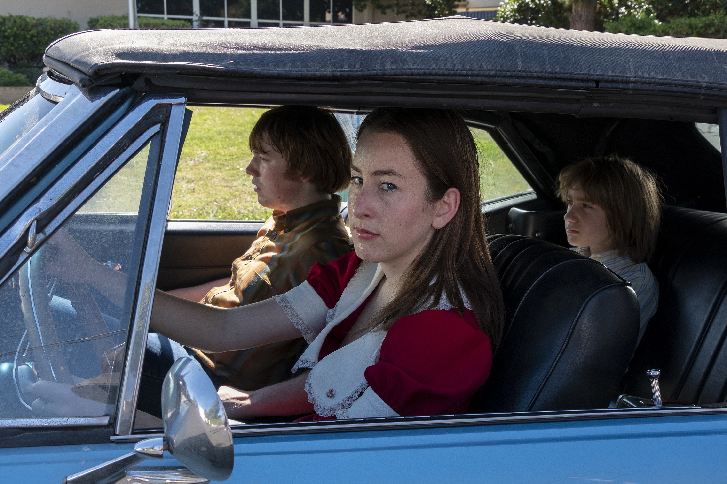 Alana Haim drives a car with Cooper Hoffman sitting beside her