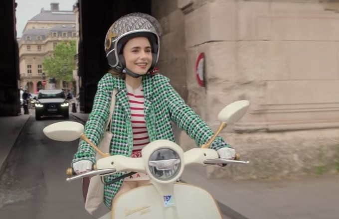 Emily riding a moped while wearing the coat and dress