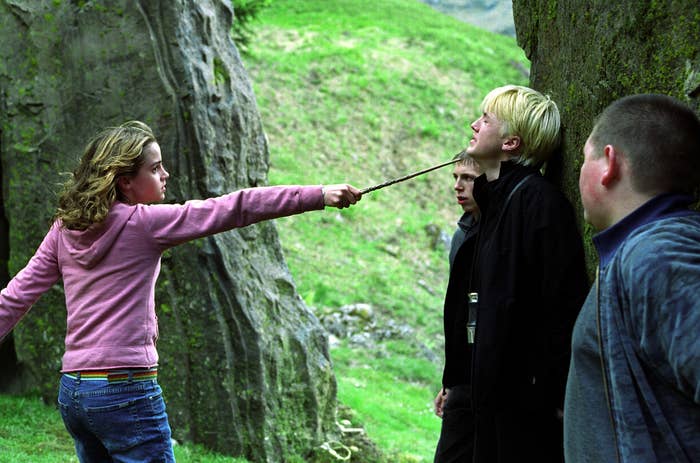 Emma points her wand at Tom's face while he's against the tree