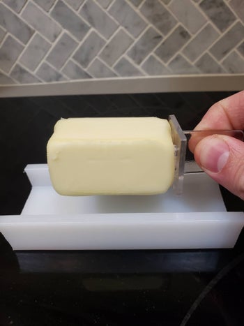 Hand picking up a slab of butter from the butter dish using the butter stick