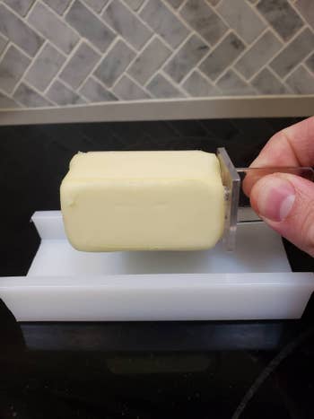 Hand picking up a slab of butter from the butter dish using the butter stick