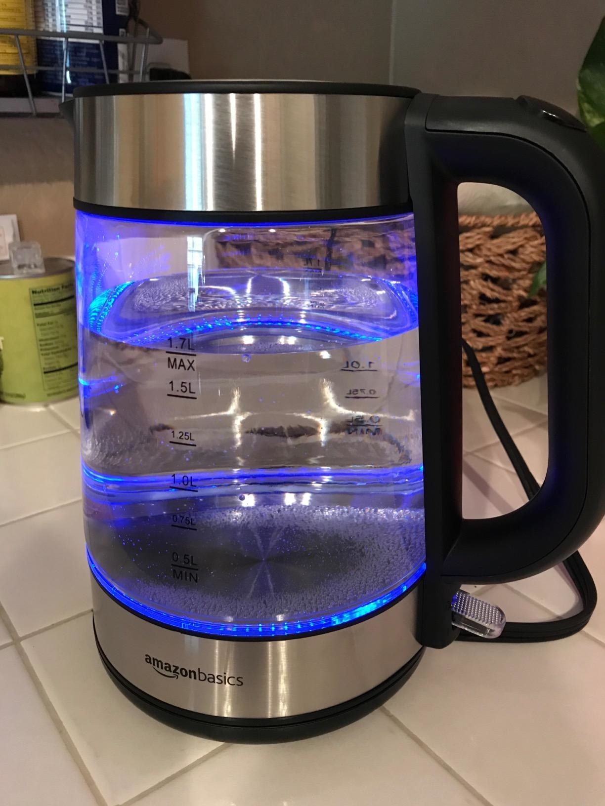A glass electric kettle with a black handle and measurements on the side plastic window