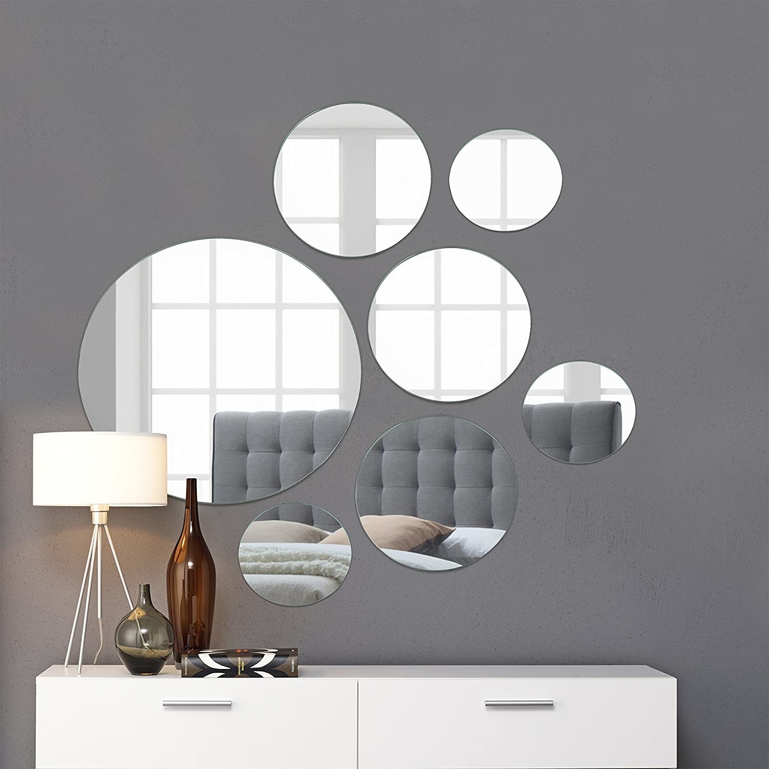 Set of seven big and small circle-shaped mirrors hanging on a green wall above a table