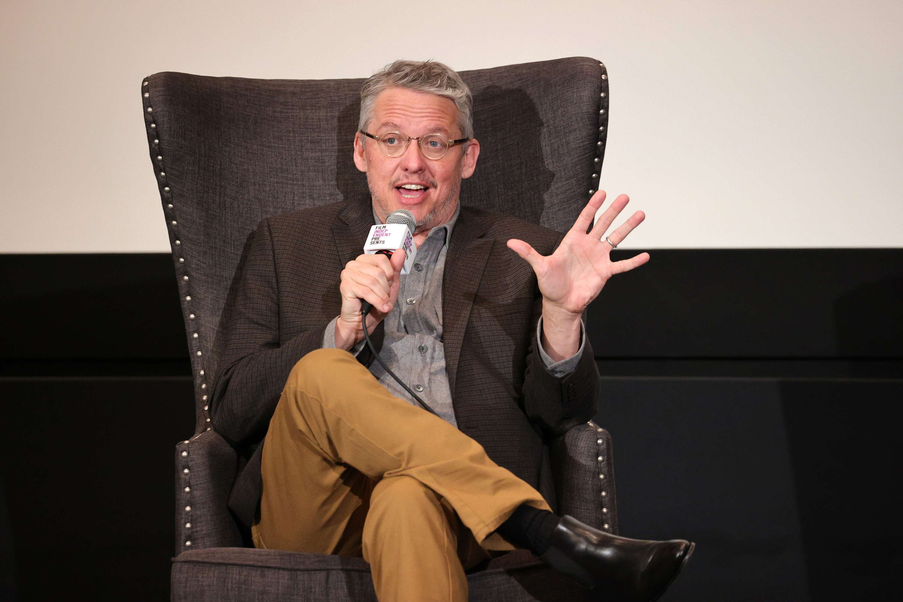 Adam McKay sitting in a chair and speaking into a microphone